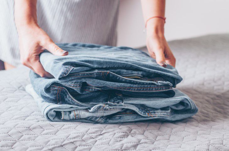 Frau faltet ihre Jeans auf einem Bett um sie zu spenden
