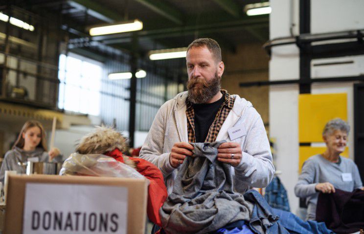 Mann mit Bart sortiert gespendete Kleidung